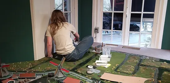 Een jonge modelbouwer zit op de Zaanse Schans-maquette om bij een lastige plek te komen